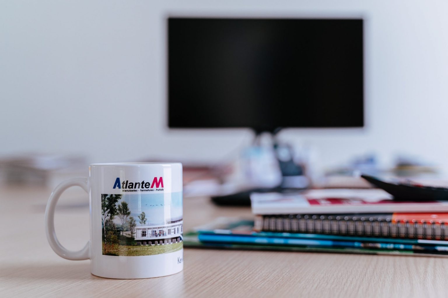 Photographie d'un mug au logo d'une entreprise avec en arrière plan l'écran d'un ordinateur