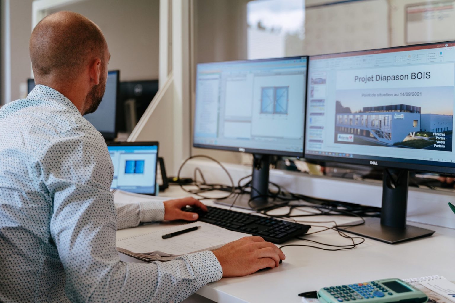 Photographie d'un homme de dos, devant son poste de travail où se trouvent deux écrans d'ordinateur