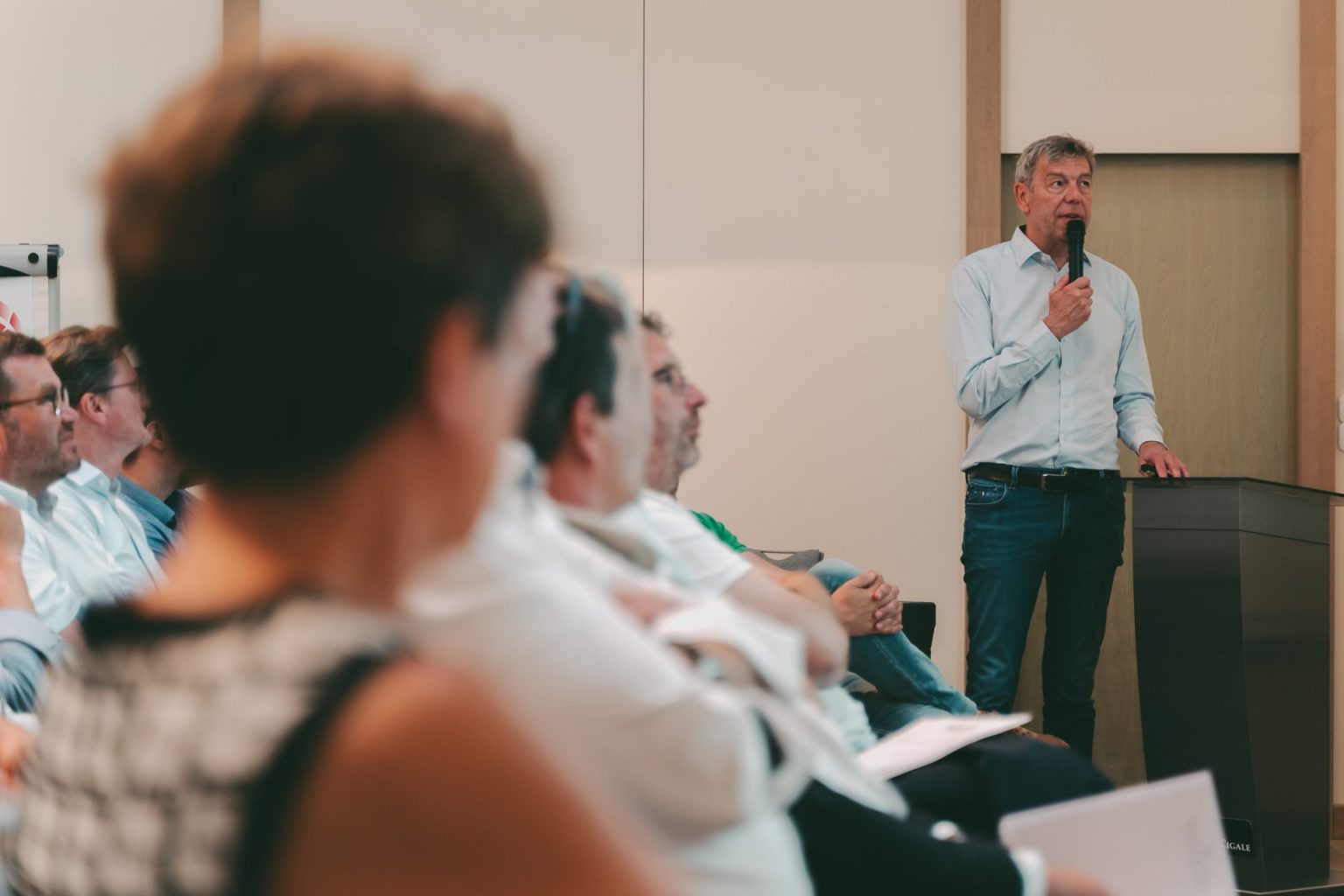 Photographie d'entreprise sur laquelle on voit une audience assiste à une réunion lors de la prise de parole d'un homme