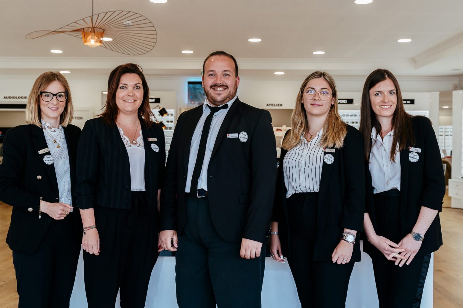 Photographie de cinq personnes habillées en tailleur noir, dans leur environnement de travail