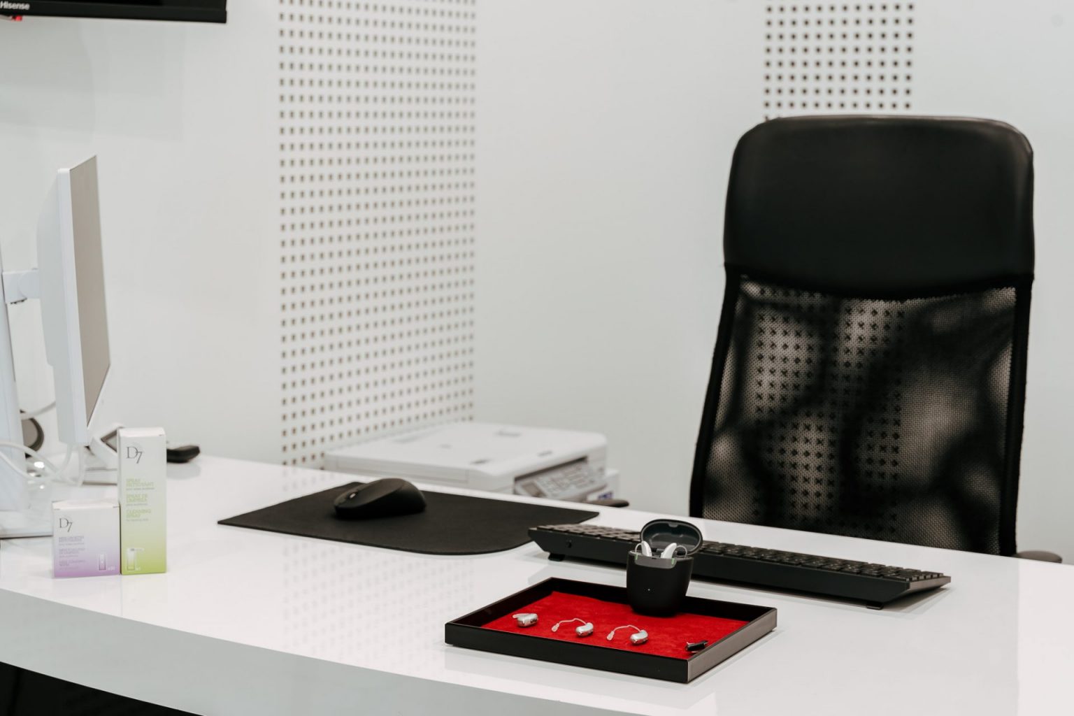 Photographie où l'on voit des appareils auditifs posés sur un petit plateau rouge sur un bureau blanc