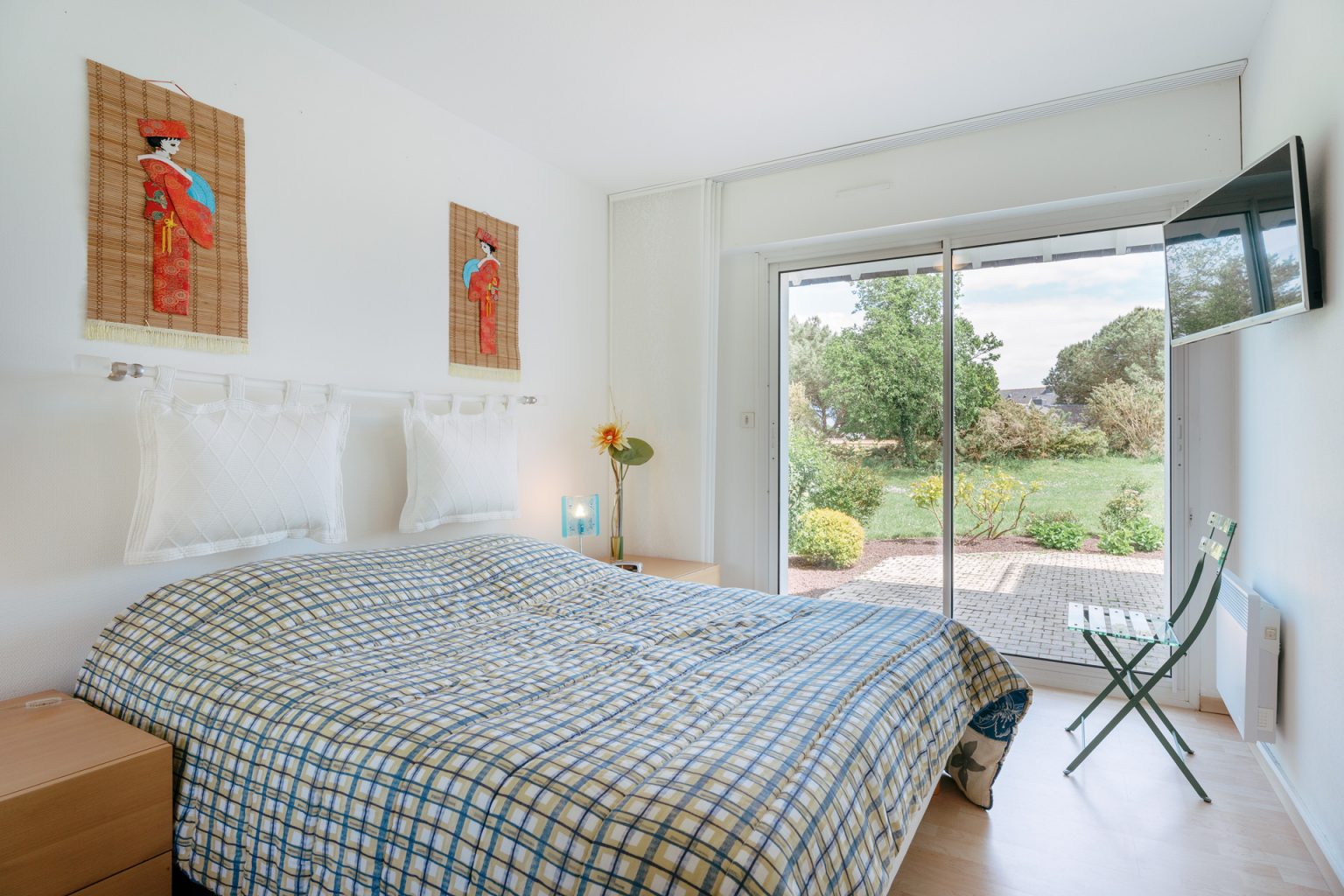 Photographie d'une chambre avec une baie vitrée donnant sur un jardin