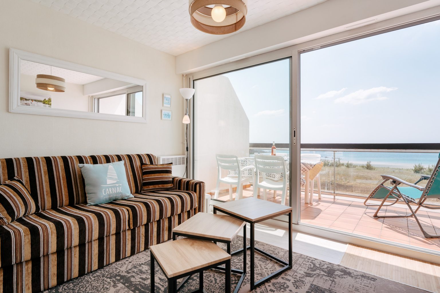 Photographie du salon d'un appartement à Carnac avec une baie vitrée donnant sur une terrasse avec une vue mer